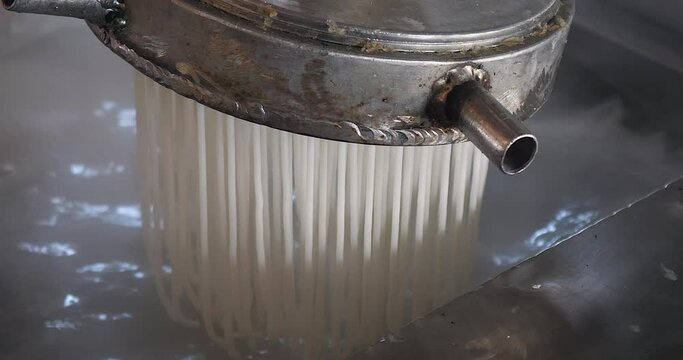 extreme close up of a machine is starting to extrude noodles into boiling water.