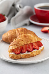 A fresh croissant with ricotta and fresh strawberries. Croissant with black coffee.