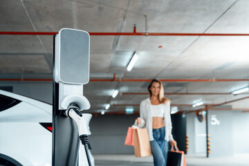 Young woman travel with EV electric car to shopping center parking lot charging in downtown city...