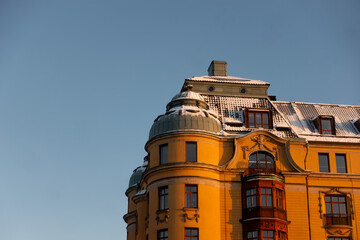 Yellow scandinavian architecture historic building in central Stockholm, Sweden with snow on roof in early morning light against blue sky background