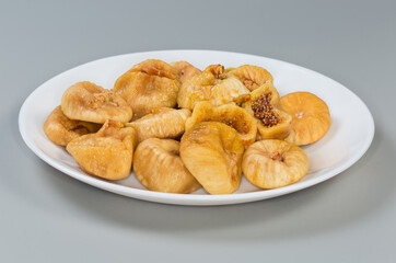 Dried figs on white dish on gray background, side view