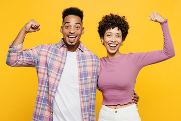 Young couple two friends family man woman of African American ethnicity wear purple casual clothes together show biceps muscles on hand demonstrating strength power isolated on plain yellow background