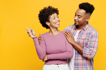 Young happy couple two friend family man woman of African American ethnicity wear purple casual clothes together point index finger aside on area hug isolated on plain yellow orange background studio
