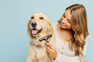 Young fun owner woman wear casual clothes hug cuddle best friend retriever dog hold grooming brush trimming isolated on plain pastel light blue background studio portrait. Take care about pet concept.