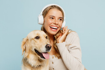 Young owner woman with her best friend retriever wear casual clothes listen to music in headphones hug cuddle dog look aside isolated on plain pastel light blue background Take care about pet concept