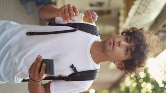 close-up portrait of an Arab male tourist in a light T-shirt in the summer walking along the city streets, eating sweet ice cream. stops and takes a photo on his smartphone.