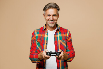 Adult fun man he wear red shirt white t-shirt casual clothes hold in hand play pc game with joystick console isolated on plain pastel light beige color background studio portrait. Lifestyle concept.