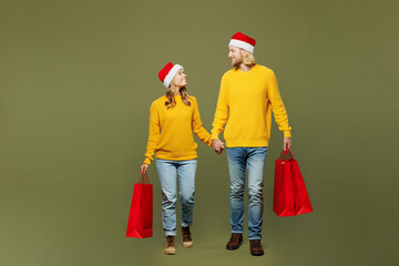 Full body merry cheerful young couple two friends man woman wears sweater Santa hat posing hold...