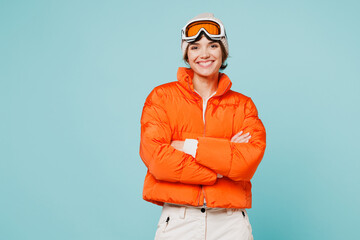 Skier smiling young woman wearing warm padded windbreaker jacket hat ski goggles mask hold hands crossed folded travel rest spend weekend winter season in mountains isolated on plain blue background. © ViDi Studio