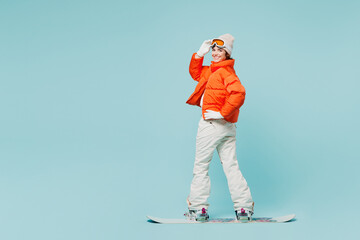 Full body sideways young woman wear warm padded windbreaker jacket hat ski goggles mask...