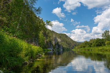 Obraz premium Calm mountain river with wooded banks. Trees hang down to the water from one bank