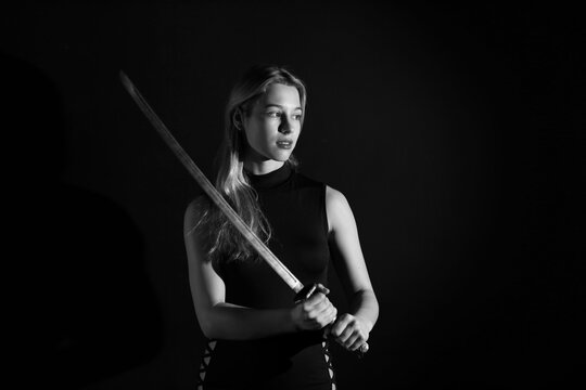 Low key portrait of young woman with katana sword in black and white