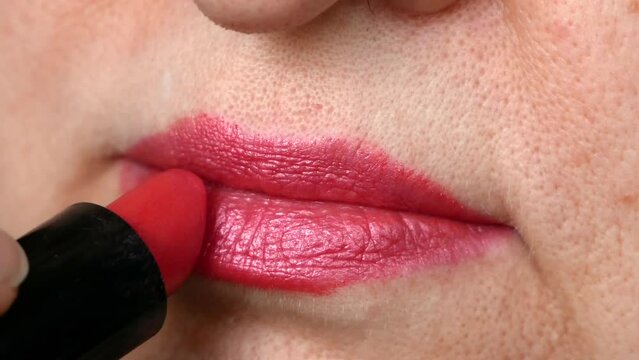  Middle-aged beautiful woman paints lips with red lipstick macro