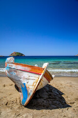 Old traditional wooden fisher boat lying on a sandy beach in Syros island, Greece