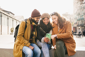 Friends sitting together using mobile phone to share content on social media in winter 
