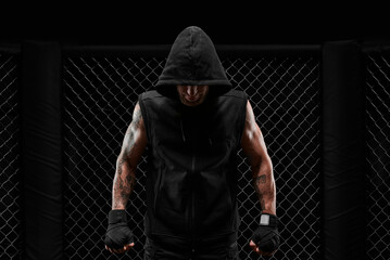 Conceptual image of a kickboxer. A real fighter stands in the real cage of the octagon. The concept of mixed idinemes, kickboxing, sports schools. - obrazy, fototapety, plakaty