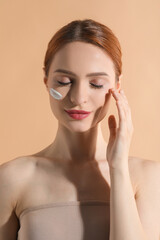 Beautiful young woman with sun protection cream on her face against beige background