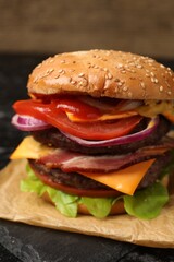 Delicious burger with meat cutlets, bacon, cheese, vegetables and lettuce on black table, closeup