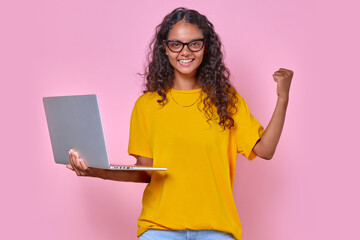 Young beautiful overjoyed Indian woman teenager holds laptop and enthusiastically waves hand after...