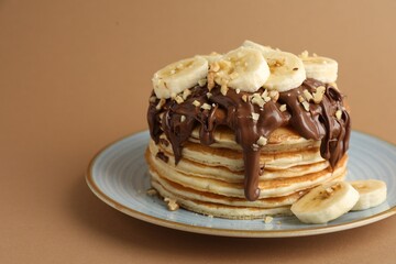 Tasty pancakes with chocolate spread, sliced banana and nuts on brown background, closeup. Space for text