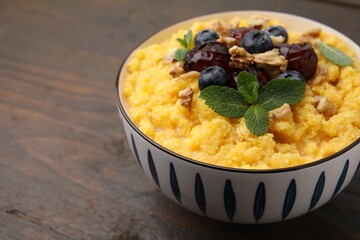 Tasty cornmeal with blueberries, dates, walnuts and mint in bowl on wooden table, closeup