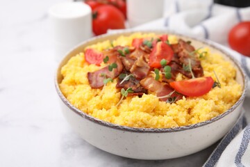 Tasty cornmeal with tomatoes, bacon and microgreens in bowl on white table, closeup. Space for text
