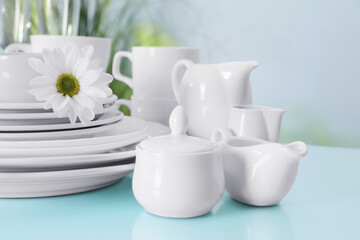 Set of clean dishware and flower on light blue table, closeup