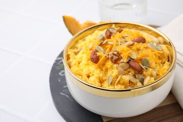 Tasty cornmeal with nuts, pumpkin and seeds in bowl on white table, closeup. Space for text