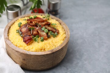 Cooked cornmeal with bacon and microgreens in bowl on light grey table, closeup. Space for text