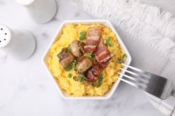 Cooked cornmeal with bacon, mushrooms and microgreens in bowl on white marble table, top view
