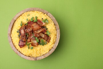 Cooked cornmeal with bacon and microgreens in bowl on light green table, top view. Space for text