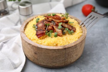 Cooked cornmeal with bacon and microgreens in bowl on light grey table, closeup