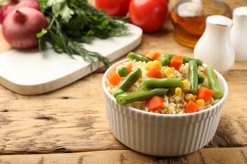 Delicious bulgur with vegetables on wooden table, closeup. Space for text