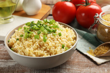 Delicious bulgur with green onion on wooden table, closeup