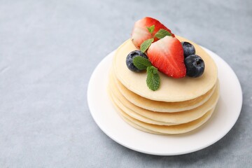 Stack of tasty pancakes with fresh berries and mint on light grey table, closeup. Space for text