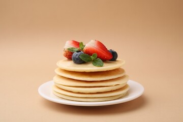Stack of tasty pancakes with fresh berries and mint on beige background