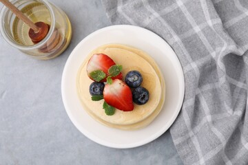 Stack of tasty pancakes with fresh berries, mint and honey on light grey table, top view