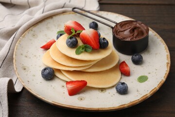 Delicious pancakes served with berries and chocolate spread on wooden table, closeup