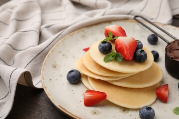 Delicious pancakes served with berries and chocolate spread on wooden table, closeup