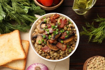 Delicious lentils with mushrooms, bacon and green onion in bowl served on wooden table, flat lay