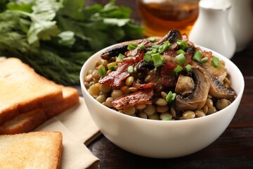Delicious lentils with mushrooms, bacon and green onion in bowl served on table, closeup