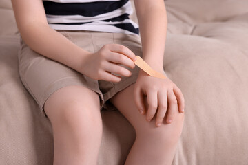 Little boy putting sticking plaster onto hand on sofa, closeup