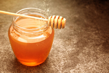 Natural honey in glass jar and dipper under sunlight, closeup. Space for text