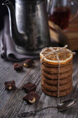 intage teapot, oatmeal cookies and chocolate chips on a wooden background. Shot in low key. Vertical image.
