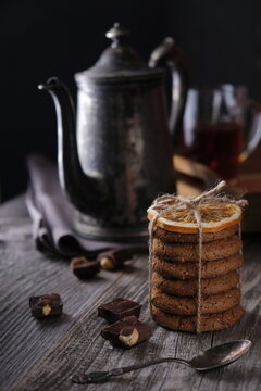 intage teapot, oatmeal cookies and chocolate chips on a wooden background. Shot in low key. Vertical image.