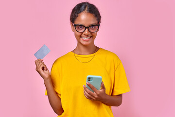 Young smiling ethnic Indian woman shopaholic uses phone for online shopping and shows credit card...