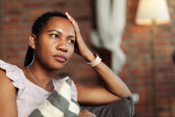 Mid adult black woman thinking of something while sitting on sofa at home