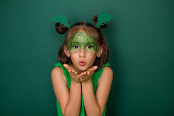 An attractive girl with a dragon scale pattern on her face, on a green studio background, sends an...