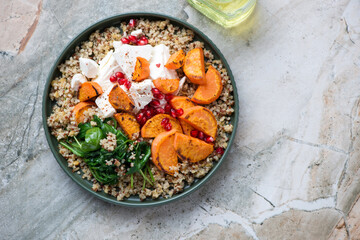 Quinoa with feta, roasted sweet potato, pomegranate and wilted spinach, top view on a grey granite background, horizontal shot with copyspace
