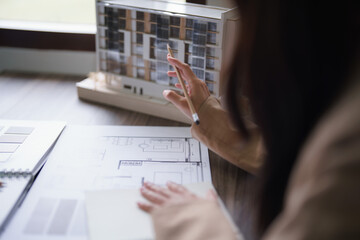 Female architect looking on building model and designing architecture interior project on blueprint